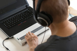 Mężczyzna w słuchawkach używa komputera z przystawjką brajlowską